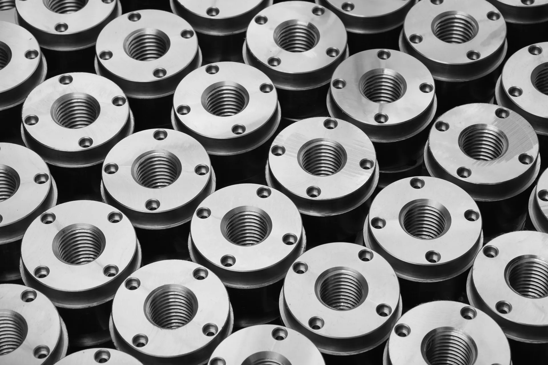 Yan yana dizilmiş, iç dişi ve delikleri işlenmiş özdeş tornalanmış metal parçaların üstten görünümü