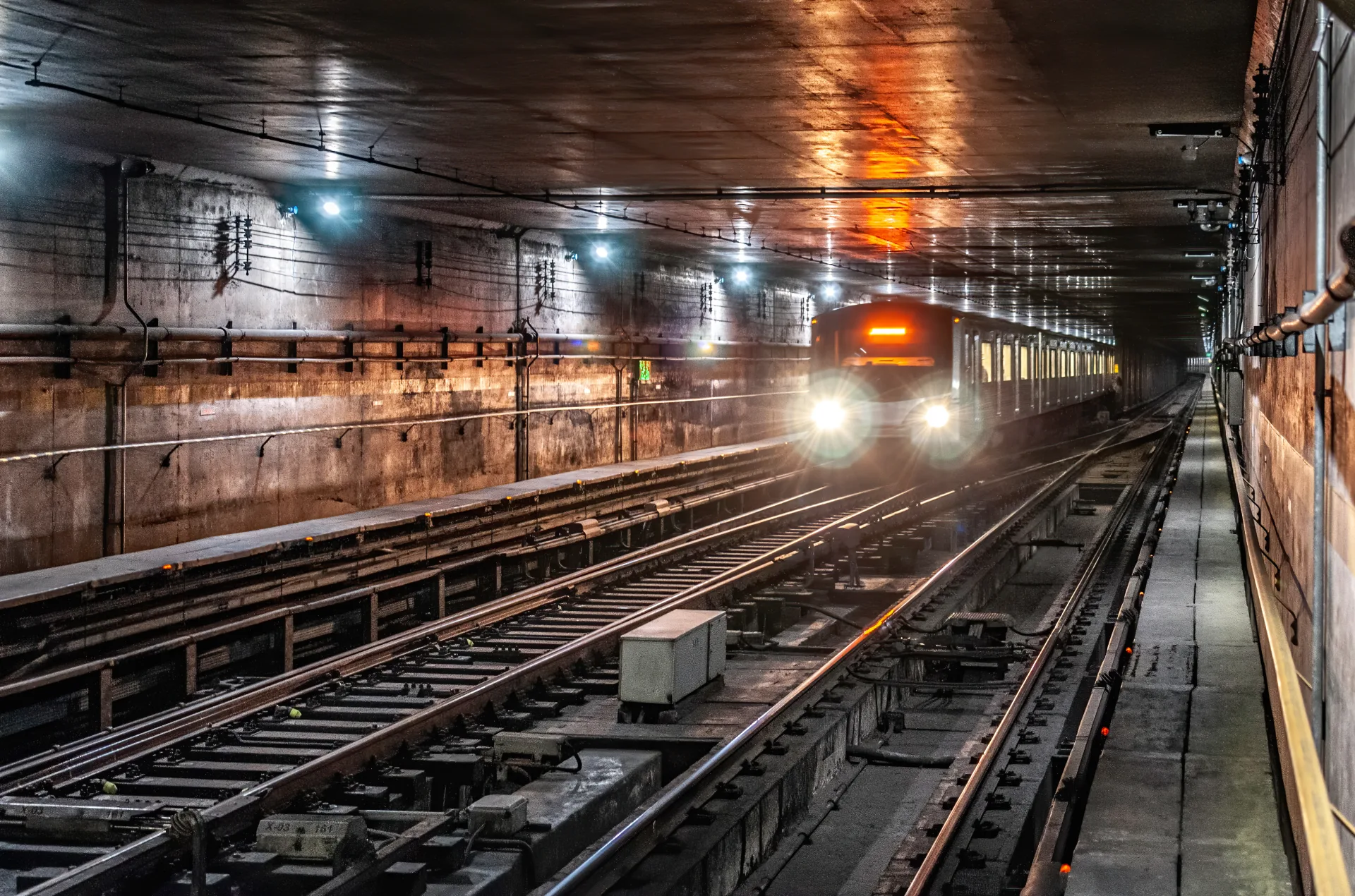 Tünelde farları yanan metro treni yaklaşırken ön planda çelik raylar ve makaslar