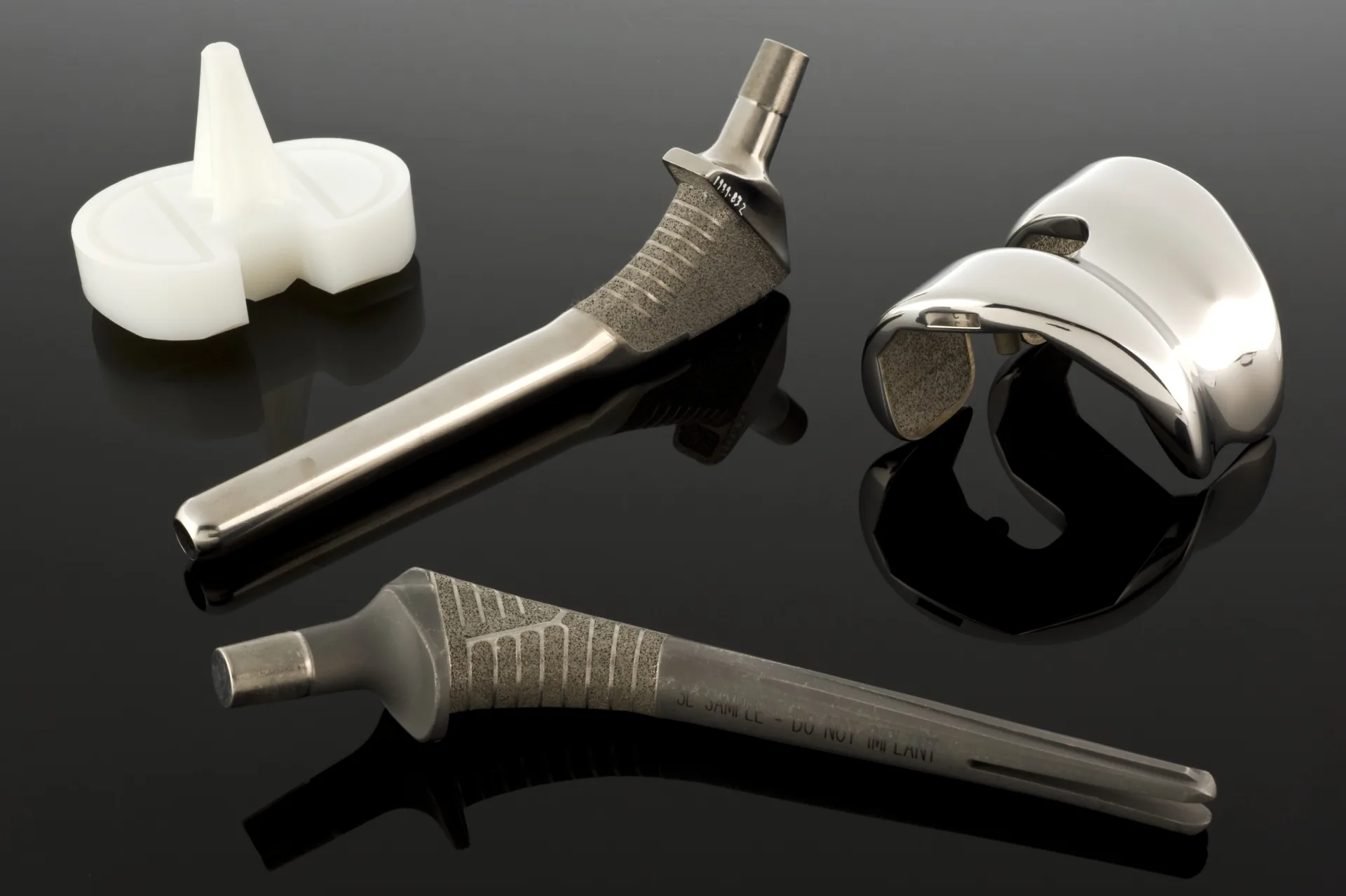 Siyah yansıtıcı zeminde titanyum kalça protezi sapları ve parlak metal eklem implantı